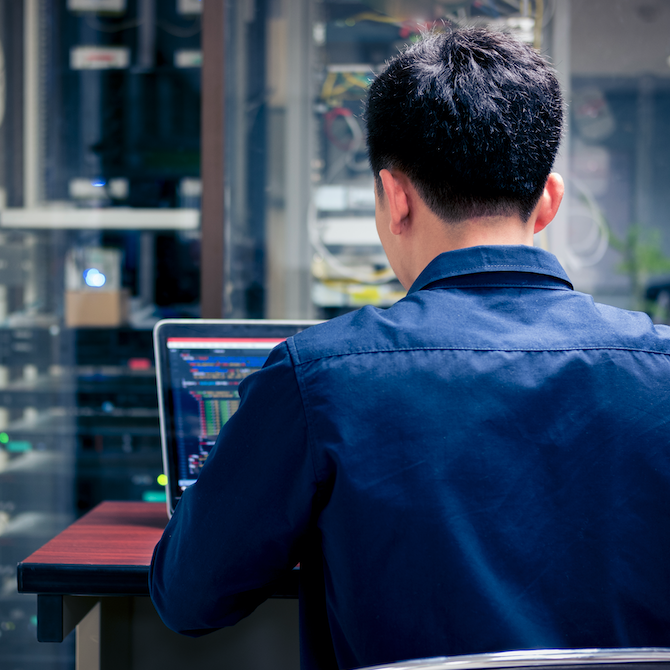 Man working on laptop with server in background